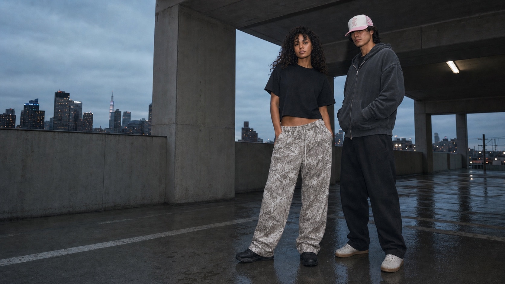 Two models wearing Iron Entity pieces beneath a concrete structure at dusk